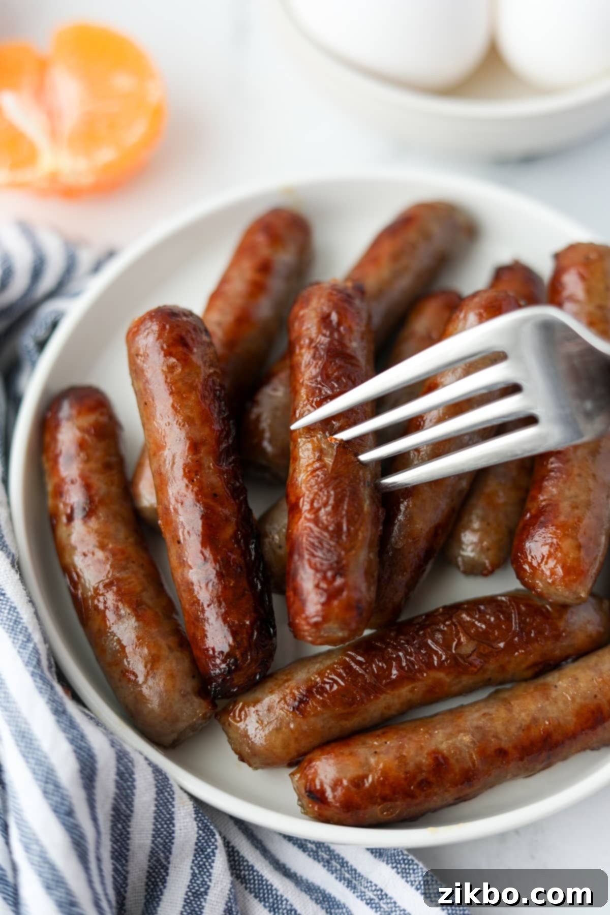 A fork taking a small, perfectly cooked sausage link from a plate, highlighting its crispy exterior.
