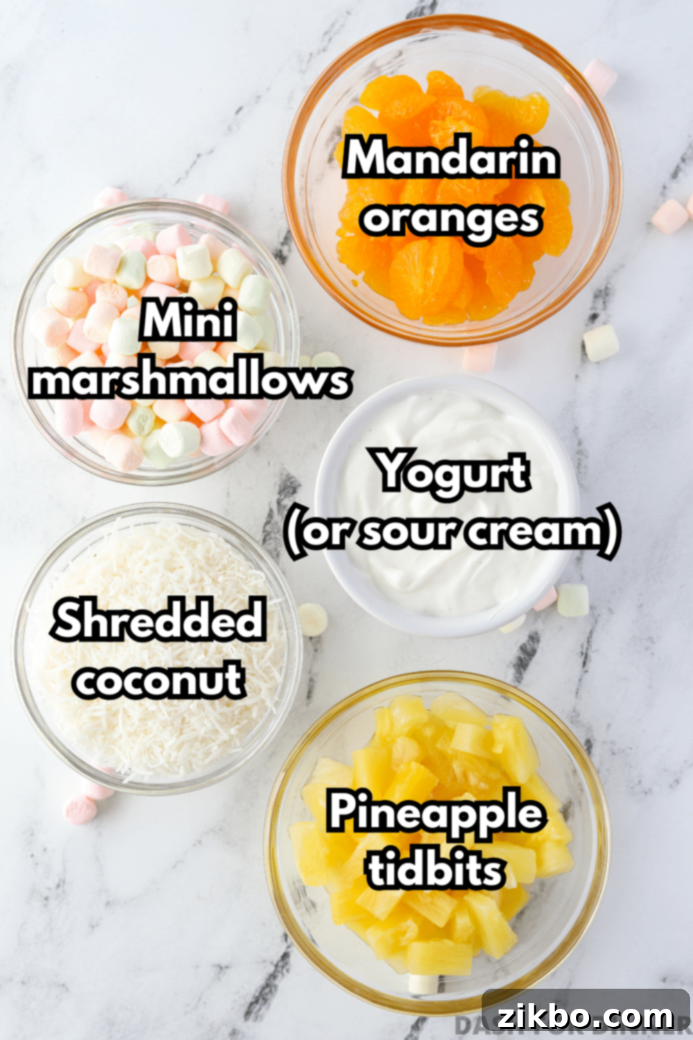 An overhead view of 5 bowls: mandarin oranges, mini marshmallows, yogurt, shredded coconut, and pineapple.