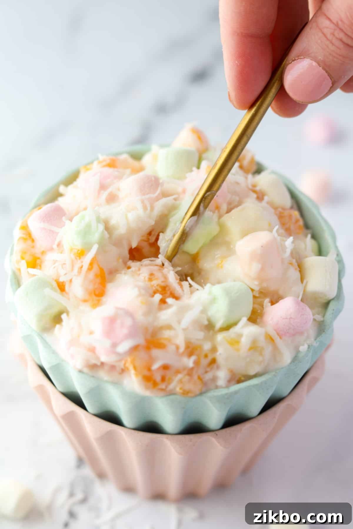 A hand taking a spoonful of marshmallow fruit salad.