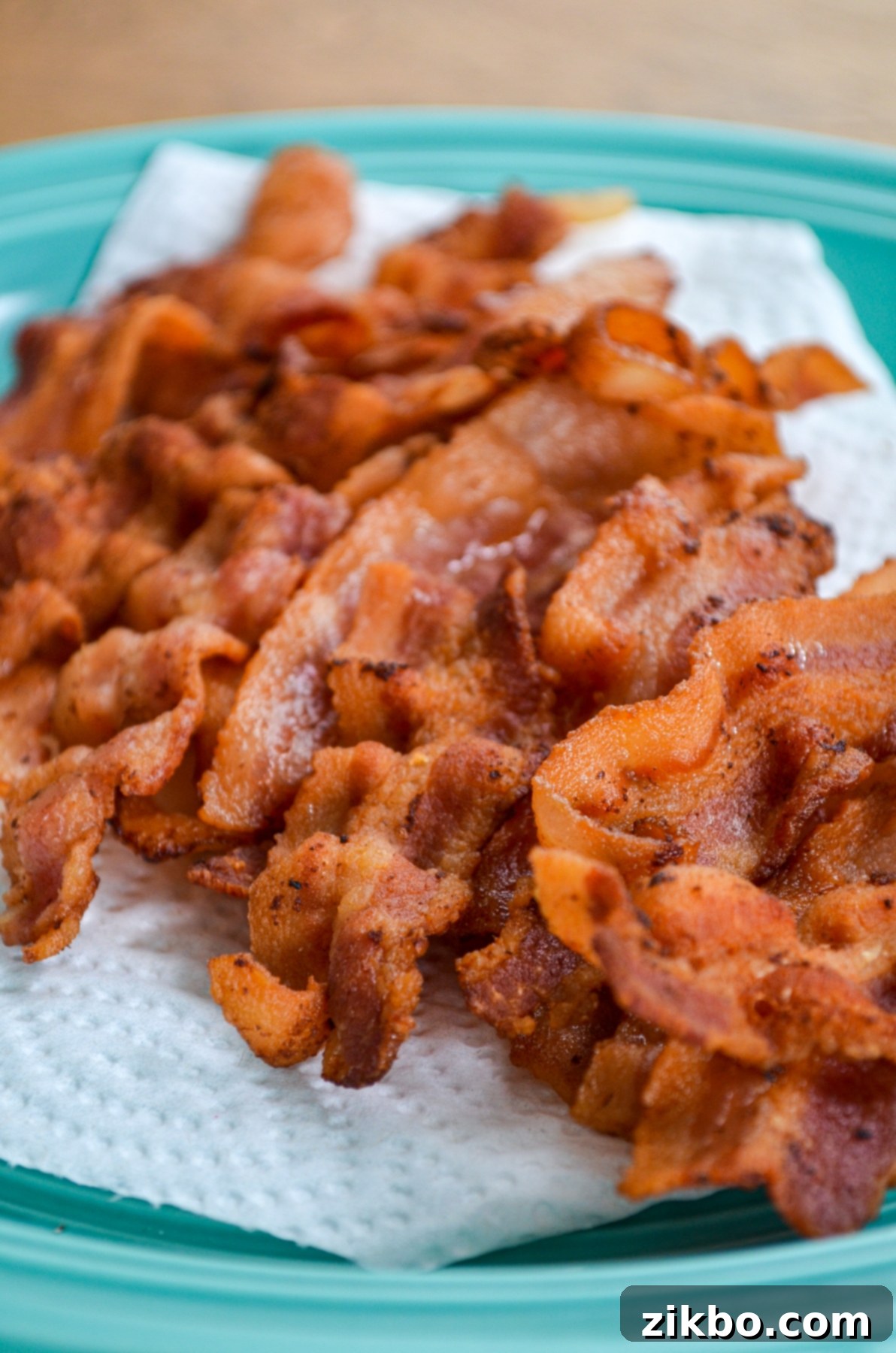 Instant Pot Bacon Slices, crispy and draining on a paper towel lined plate, showing less grease.