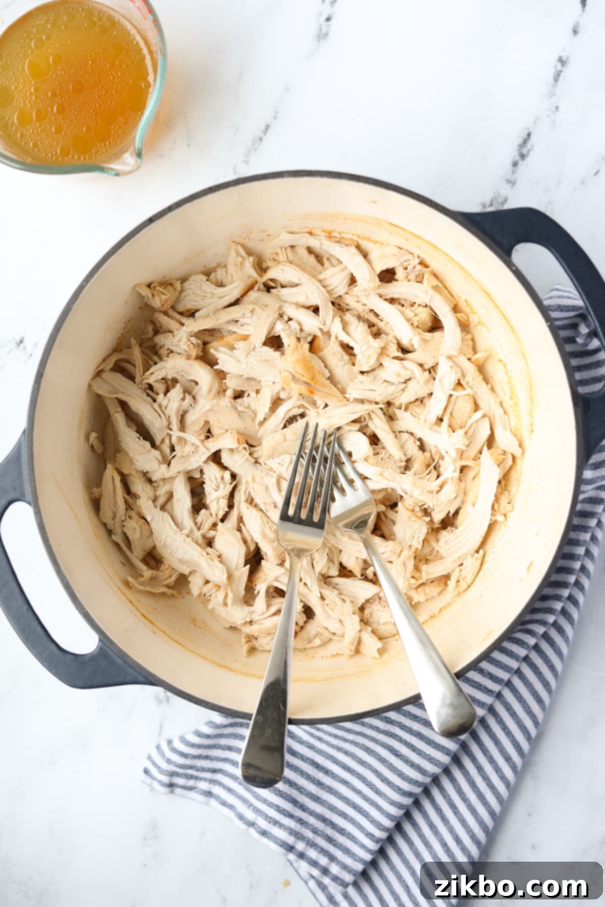 A Dutch Oven with two forks and shredded chicken, ready to be served.