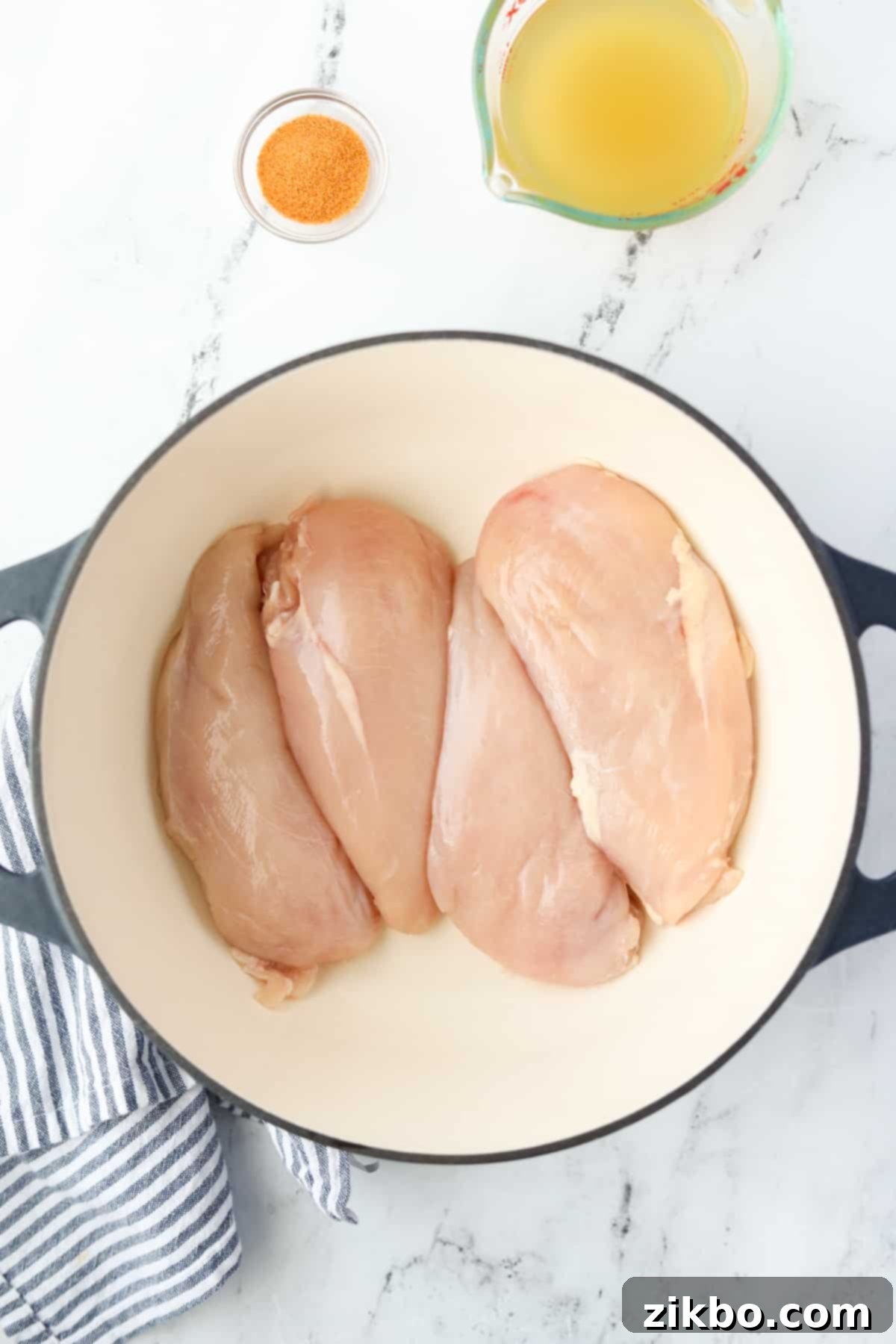 A Dutch Oven with four raw chicken breasts inside, arranged in a single layer.