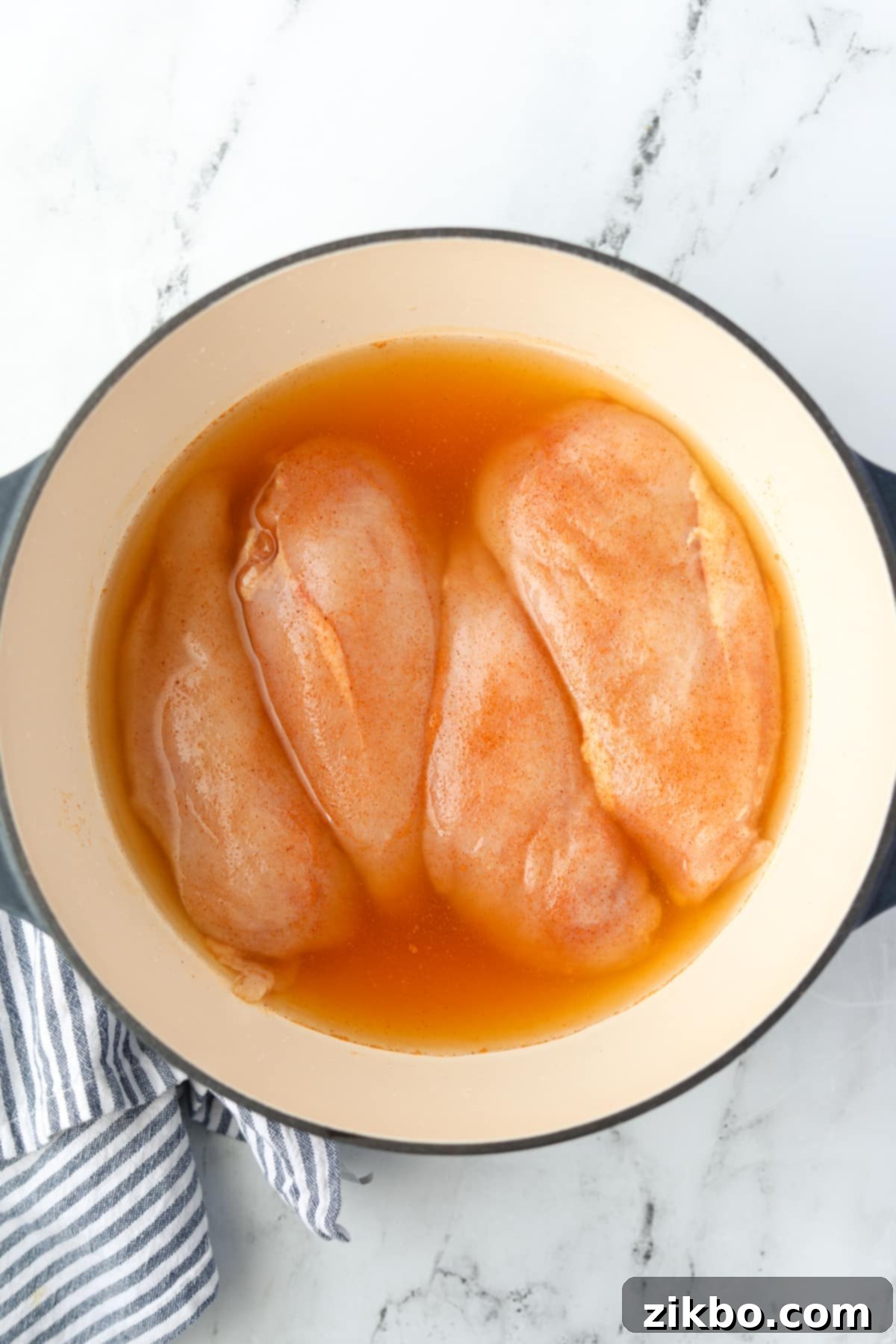 A Dutch Oven with seasoned chicken breasts partially covered with chicken broth.
