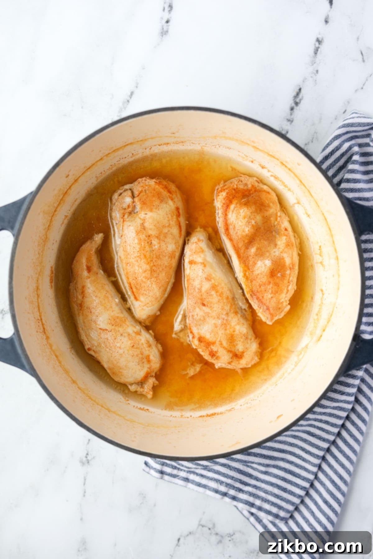 Perfectly cooked chicken breasts submerged in a simmering poaching liquid within a Dutch oven.