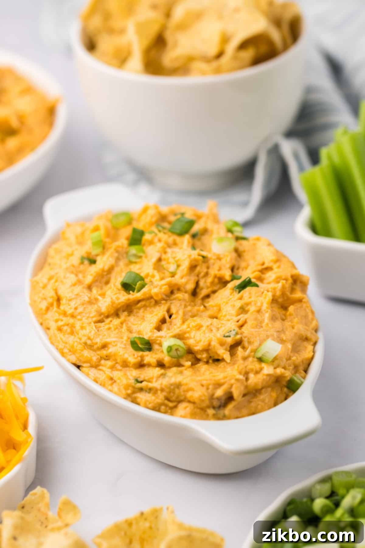 An oval baking dish filled with a hot, bubbly, and cheesy slow cooker buffalo chicken dip, garnished with green onions.