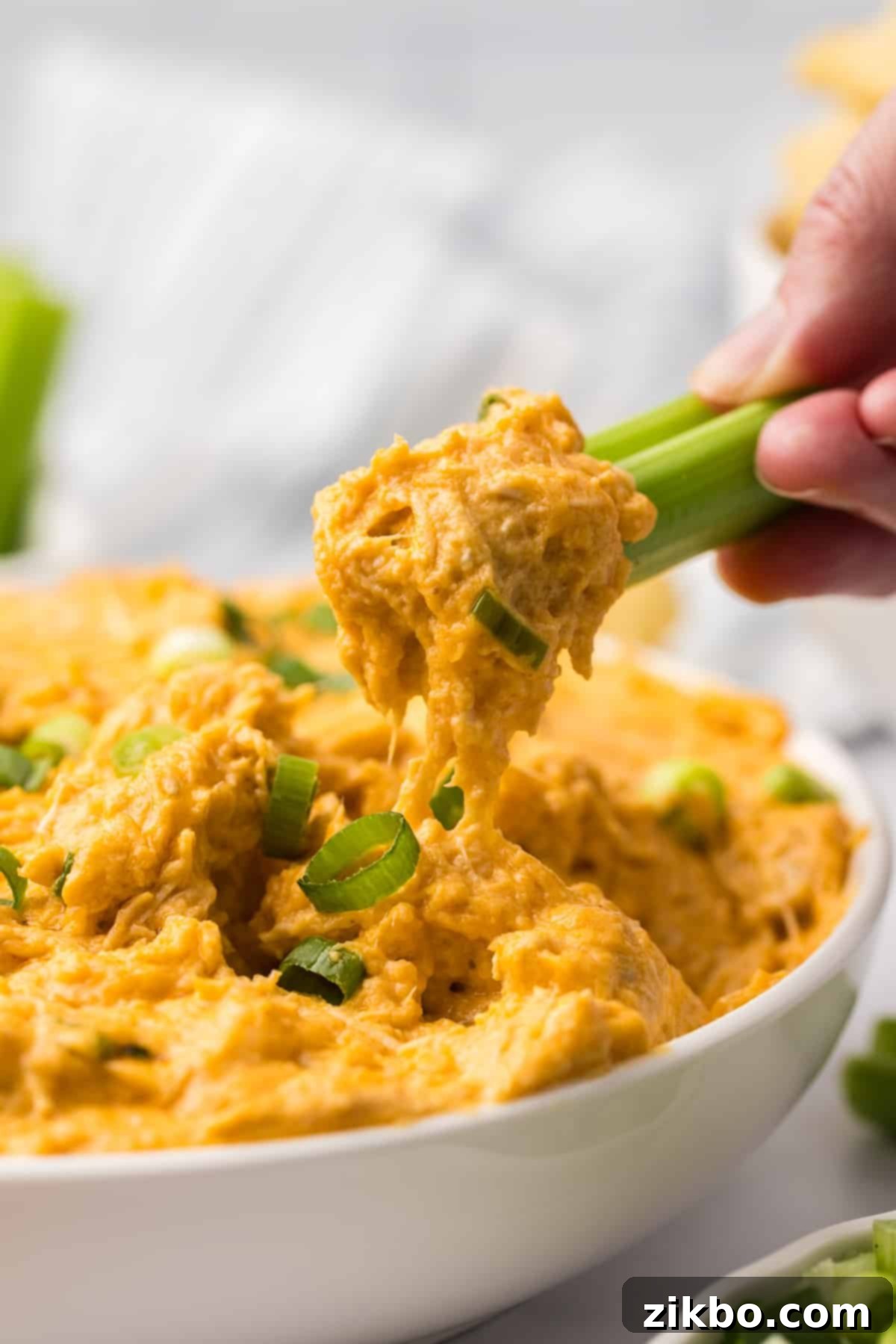 A fresh celery stick being dipped into a bowl of warm, creamy buffalo chicken dip, showing the perfect consistency.