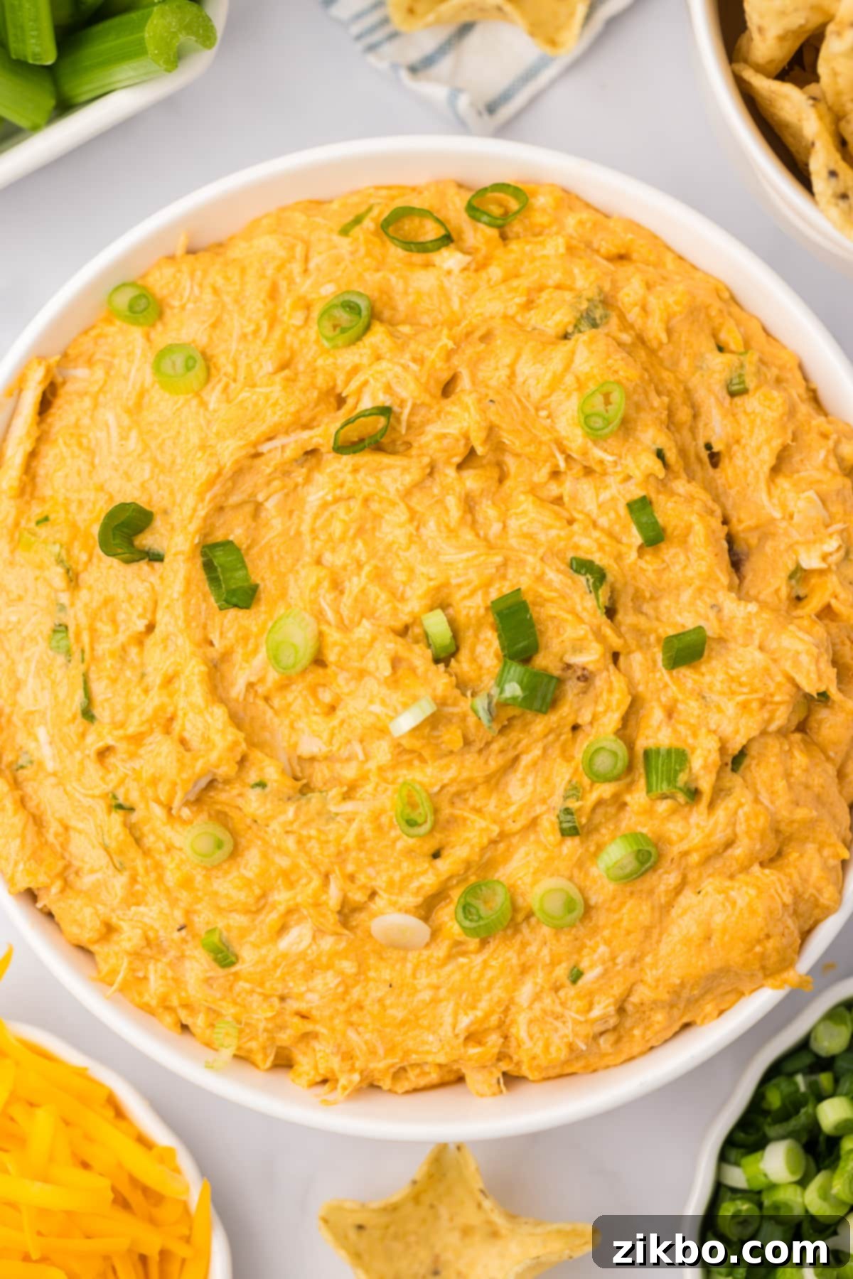 A close-up shot of a bowl of buffalo chicken dip, richly garnished with fresh chopped green onions, ready for a party.