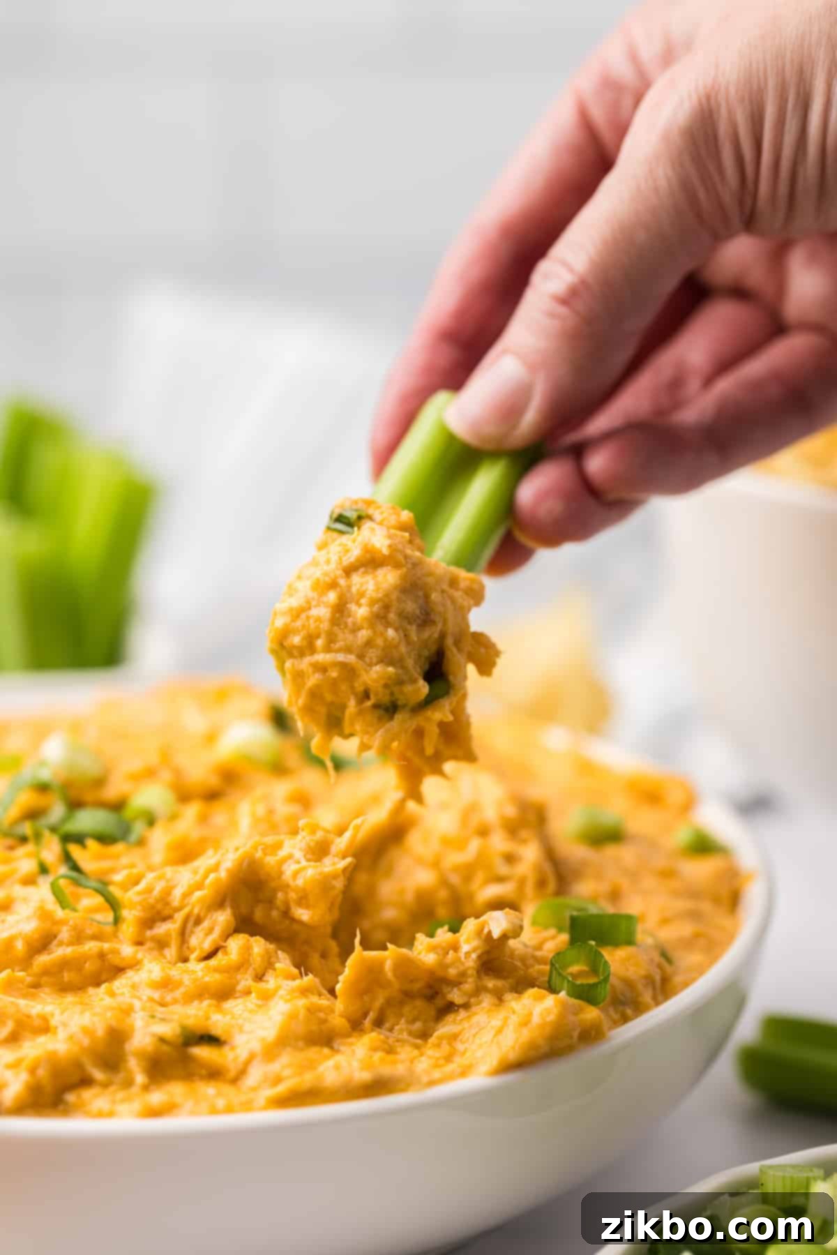 A celery stick being dipped into a bowl of creamy, hot buffalo chicken dip, highlighting the perfect appetizer for sharing.