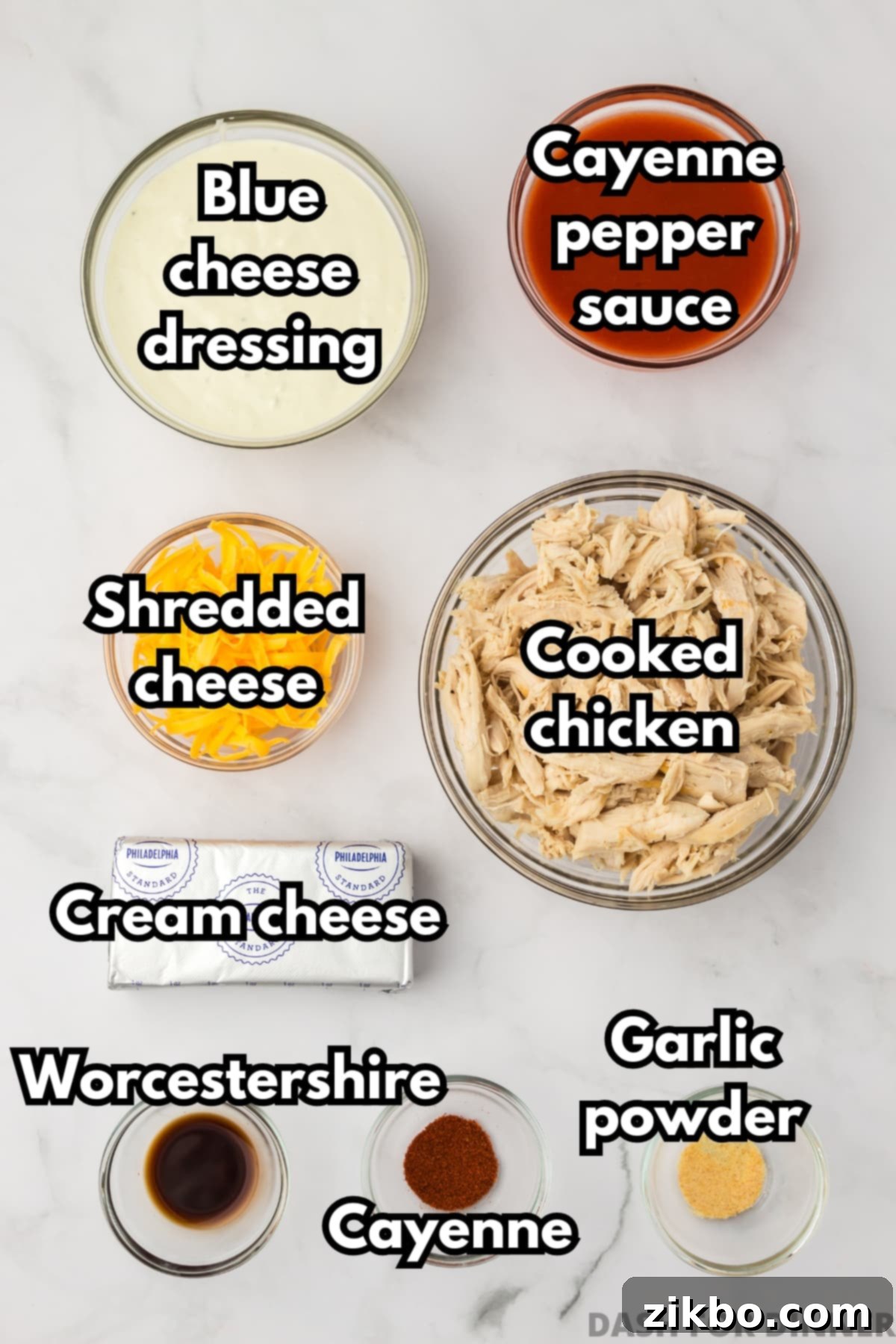 The essential ingredients laid out for making buffalo chicken dip: softened cream cheese blocks, a bottle of cayenne pepper sauce, blue cheese dressing, a block of cheddar cheese, and a bowl of cooked shredded chicken.