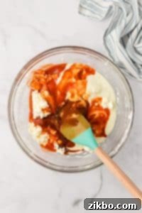 A glass bowl filled with a cream cheese mixture, with cayenne pepper sauce inside.