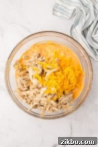 A bowl filled with a dip mixture, with shredded cheese and cooked chicken on top.
