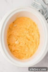 A white crock pot filled with a cheesy chicken dip.