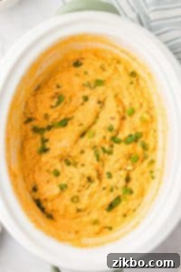 A white crock pot with a cheesy chicken dip inside.