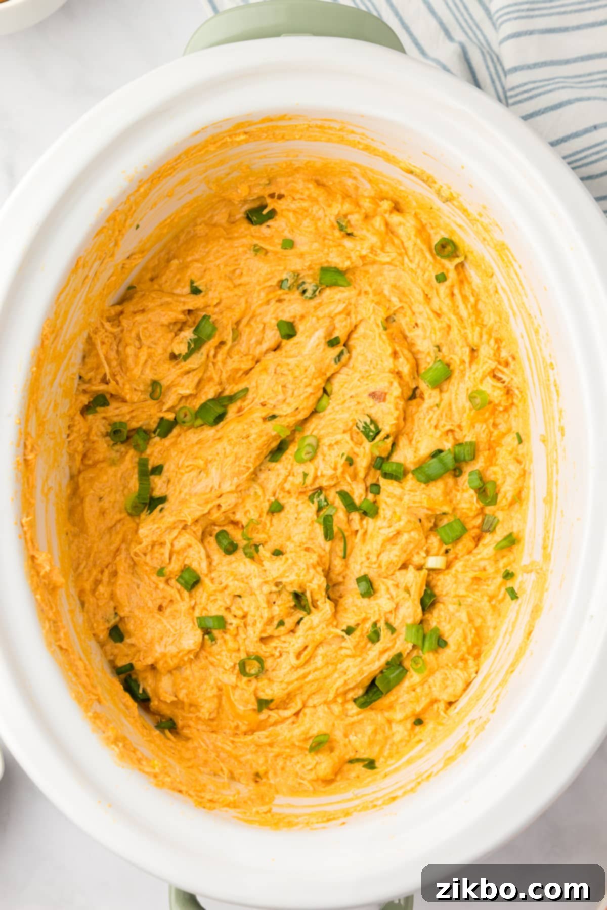A white slow cooker pot containing the hot, cheesy, and fully cooked buffalo chicken dip, ready to be served.