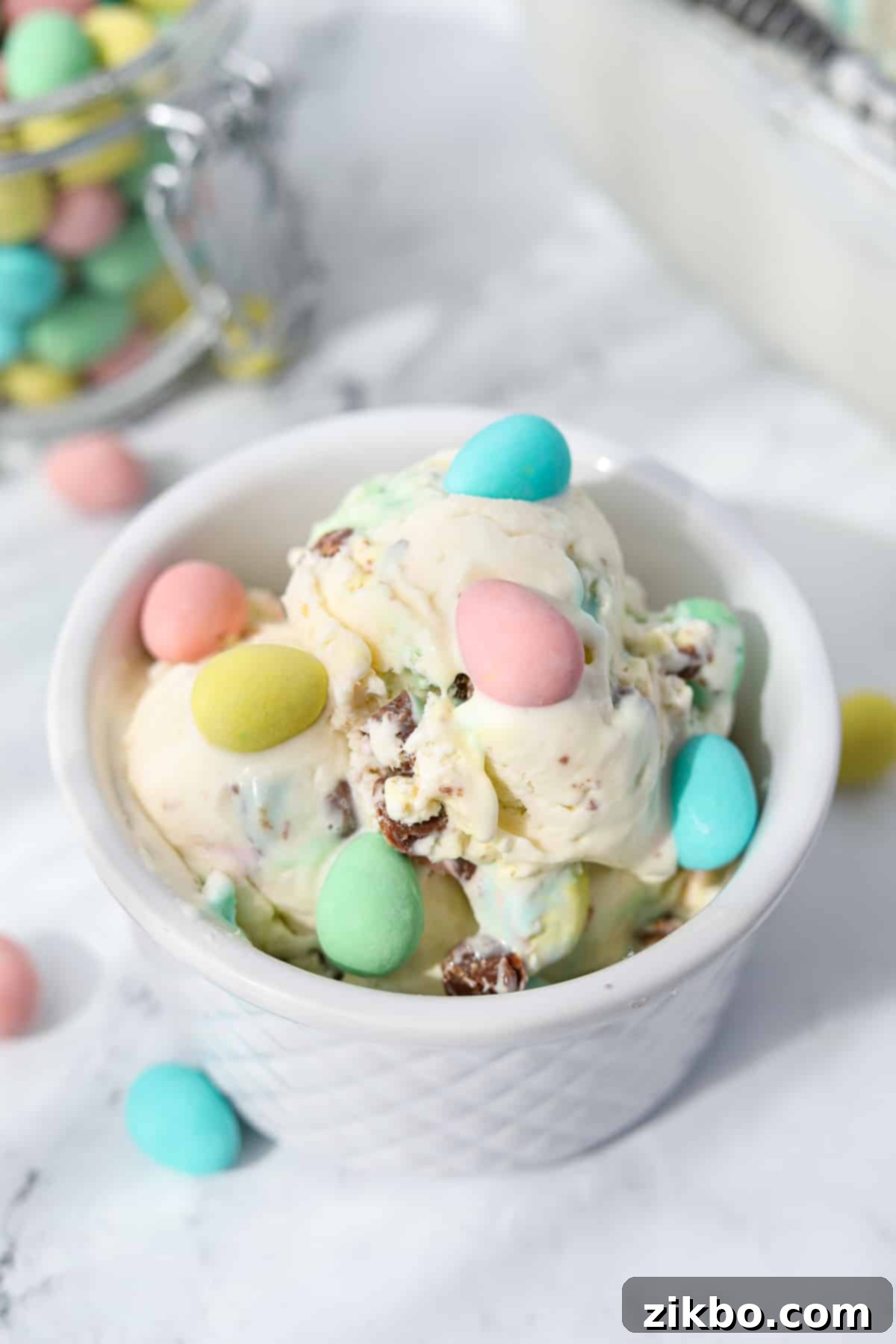 Pastel Egg Crunch Ice Cream 7 A close-up of a small white bowl filled with creamy Mini Egg Ice Cream, topped with a few colorful whole Cadbury Mini Eggs, showcasing its delightful appearance.