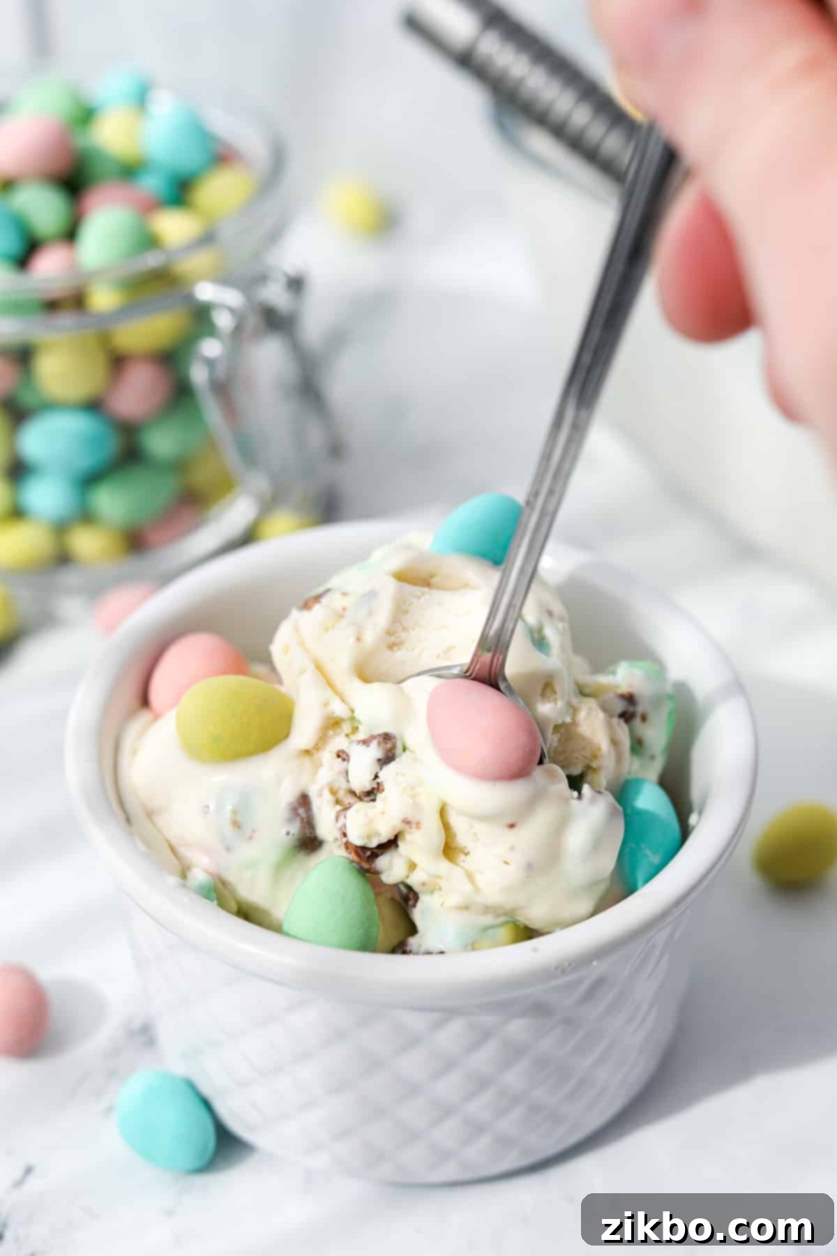 Pastel Egg Crunch Ice Cream 8 A spoon scooping a generous portion of creamy homemade Mini Egg Ice Cream from a small bowl, highlighting its smooth texture and visible mini egg pieces.
