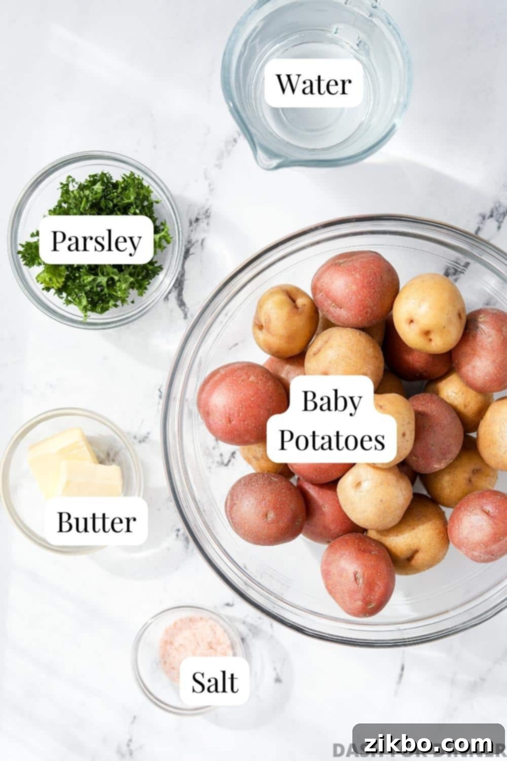 A bowl of baby potatoes, with bowls of butter, salt, parsley, and water.