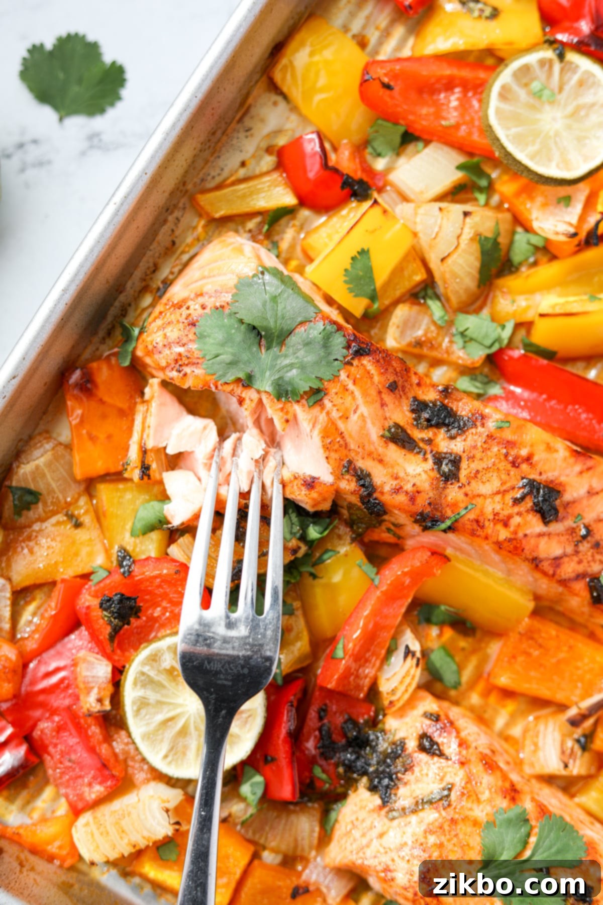 A fork taking a portion of a perfectly cooked, flaky salmon fillet from a sheet pan dinner.