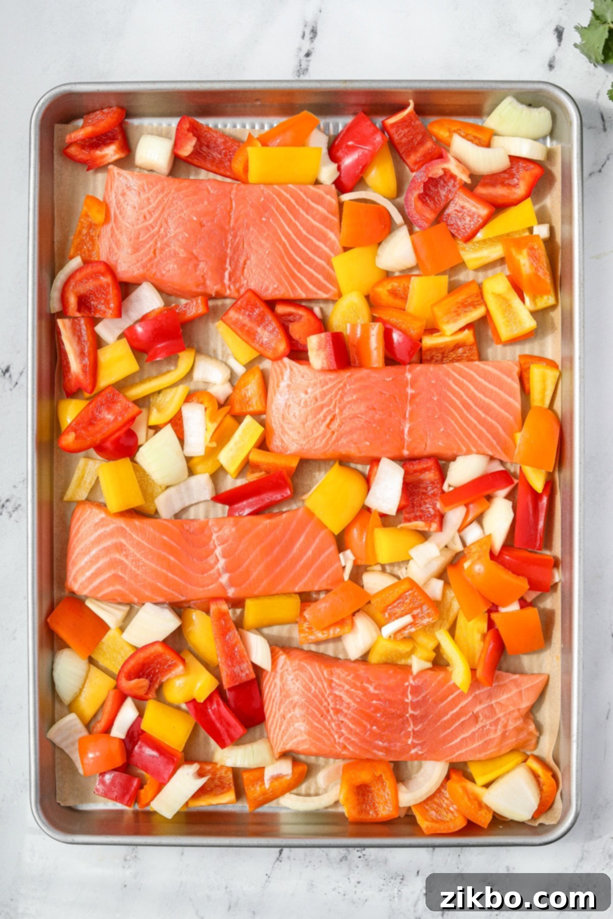 A sheet pan with raw salmon fillets and chopped bell peppers and onions, ready for the marinade.
