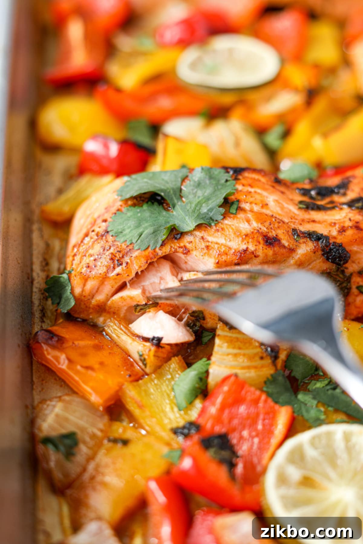 A fork flaking a piece of cooked cilantro lime salmon on a sheet pan, showing its perfect doneness.