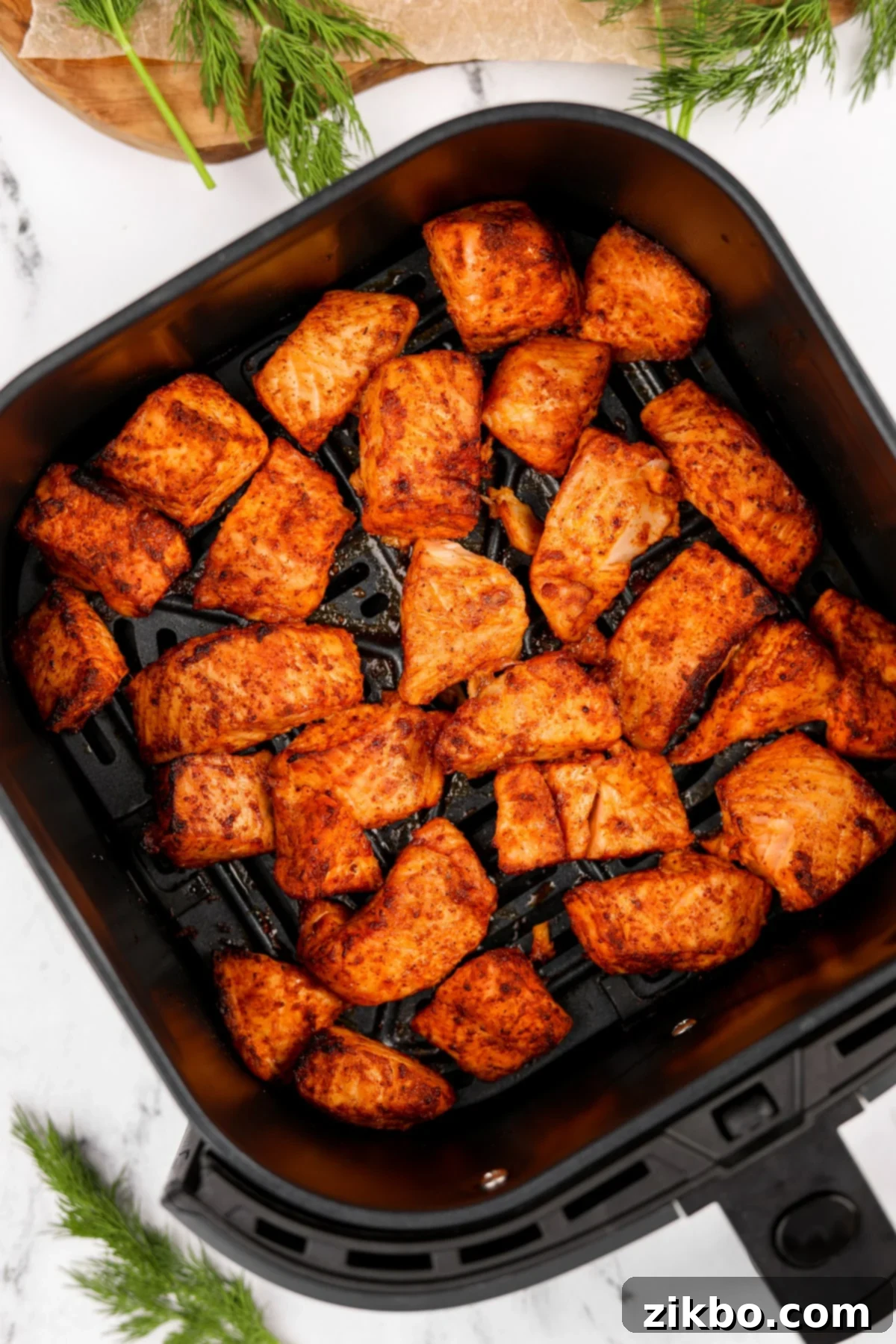 An air fryer basket filled with cubed and cooked salmon, garnished with fresh dill.