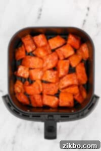 An air fryer basket filled with seasoned salmon chunks.