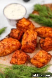 Salmon bites arranged on a plate with a small bowl of creamy dill sauce in the background.