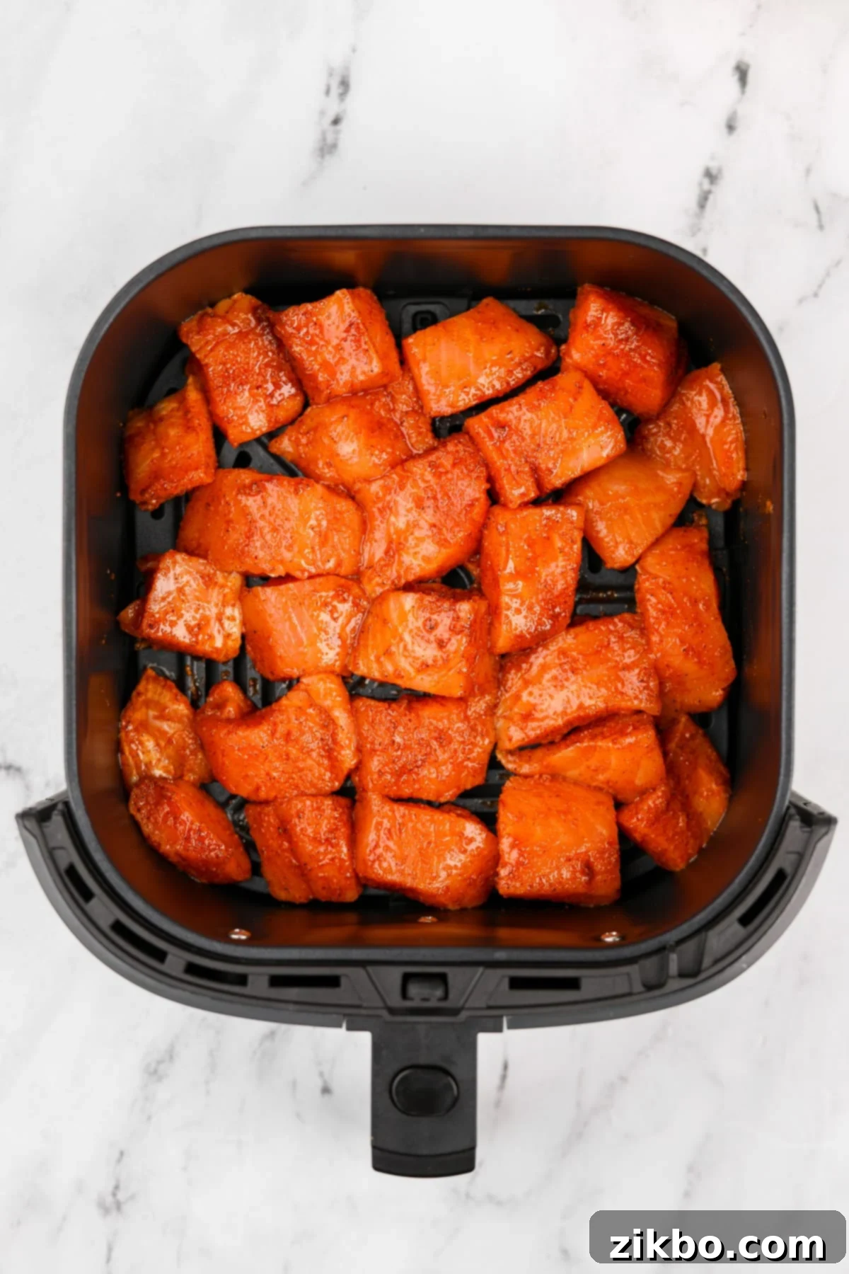 An air fryer basket loaded with seasoned salmon chunks, arranged in a single layer.
