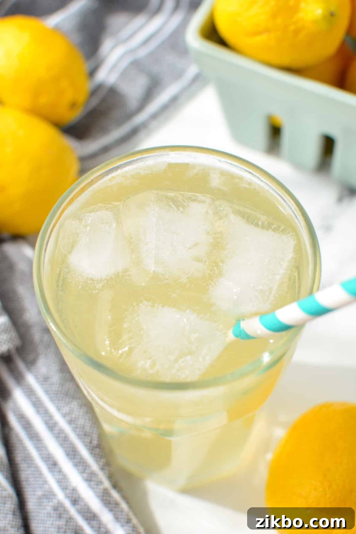 A glass of lemonade with a paper straw sticking out, condensation on the glass.