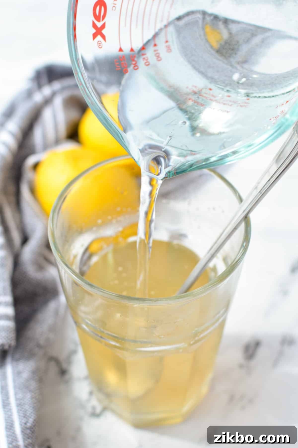 Pouring cold water into a glass with dissolved sugar mixture.