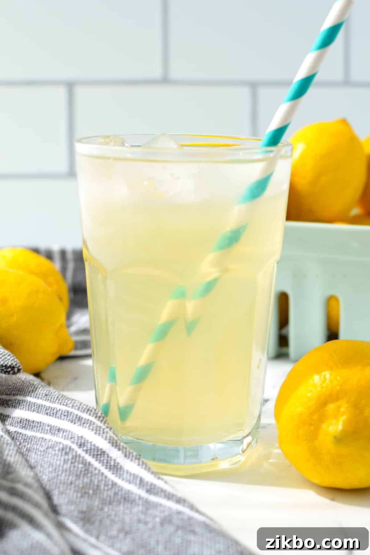 A glass of lemonade with multiple fresh lemons in the background, ready for juicing.