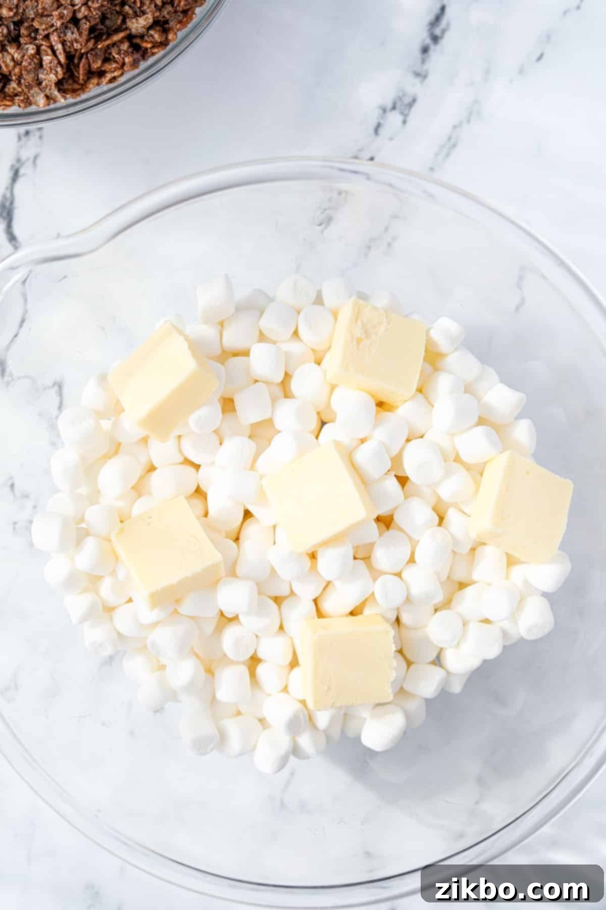 A bowl of mini marshmallows with cubed butter on top.