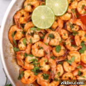 A skillet filled with cooked shrimp and garnished with cilantro and lime slices.