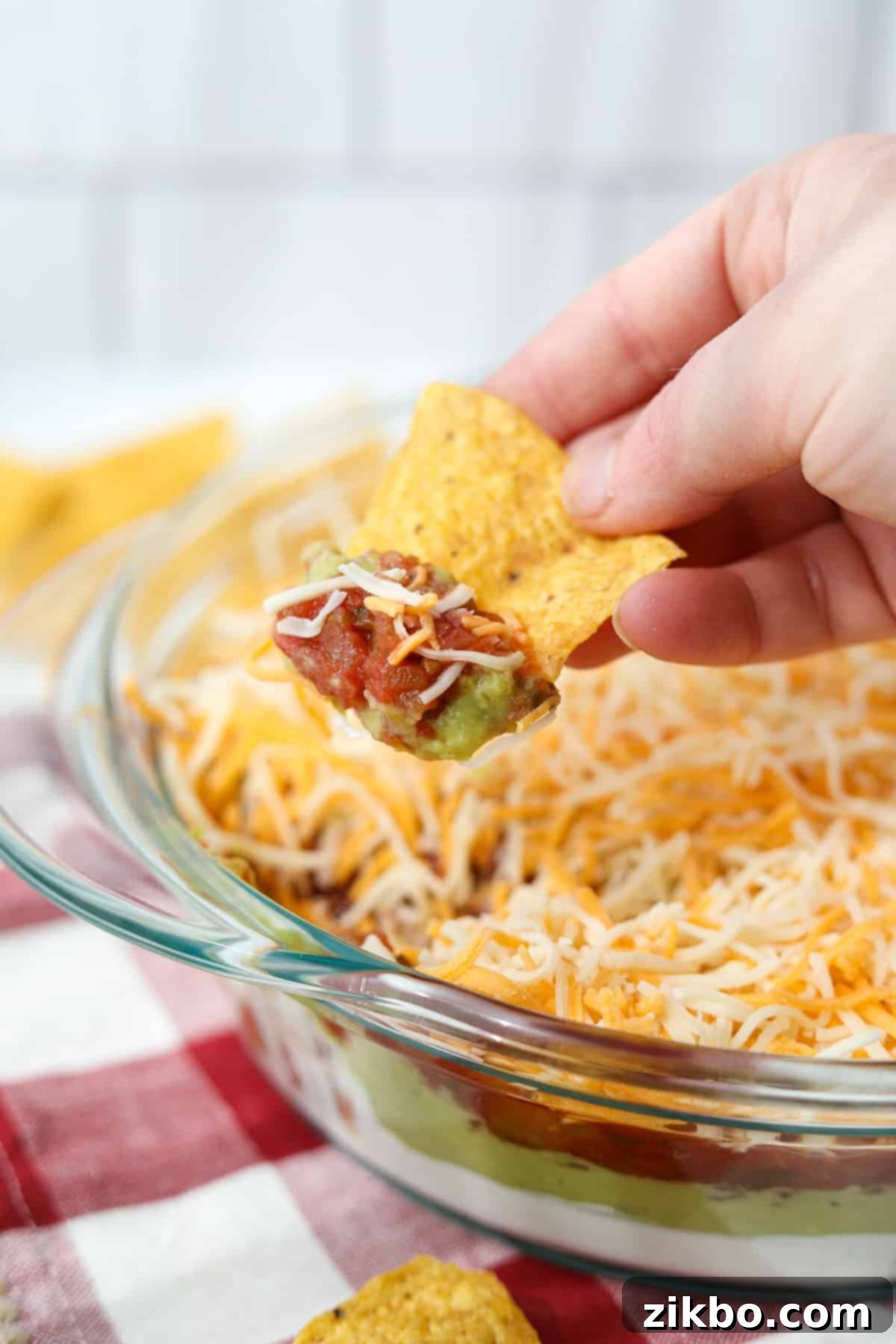 Dipping a tortilla chip into a cold 4-layer dip with sour cream, guacamole, salsa, and cheese.