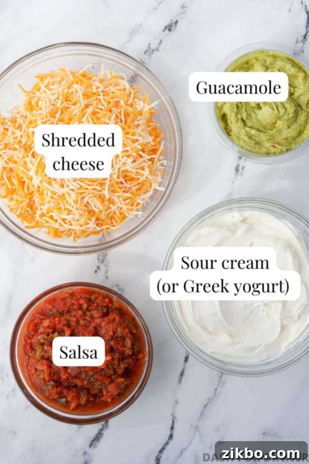 The ingredients needed to make 4 layer dip: sour cream, guacamole, salsa, and shredded cheese, arranged attractively.
