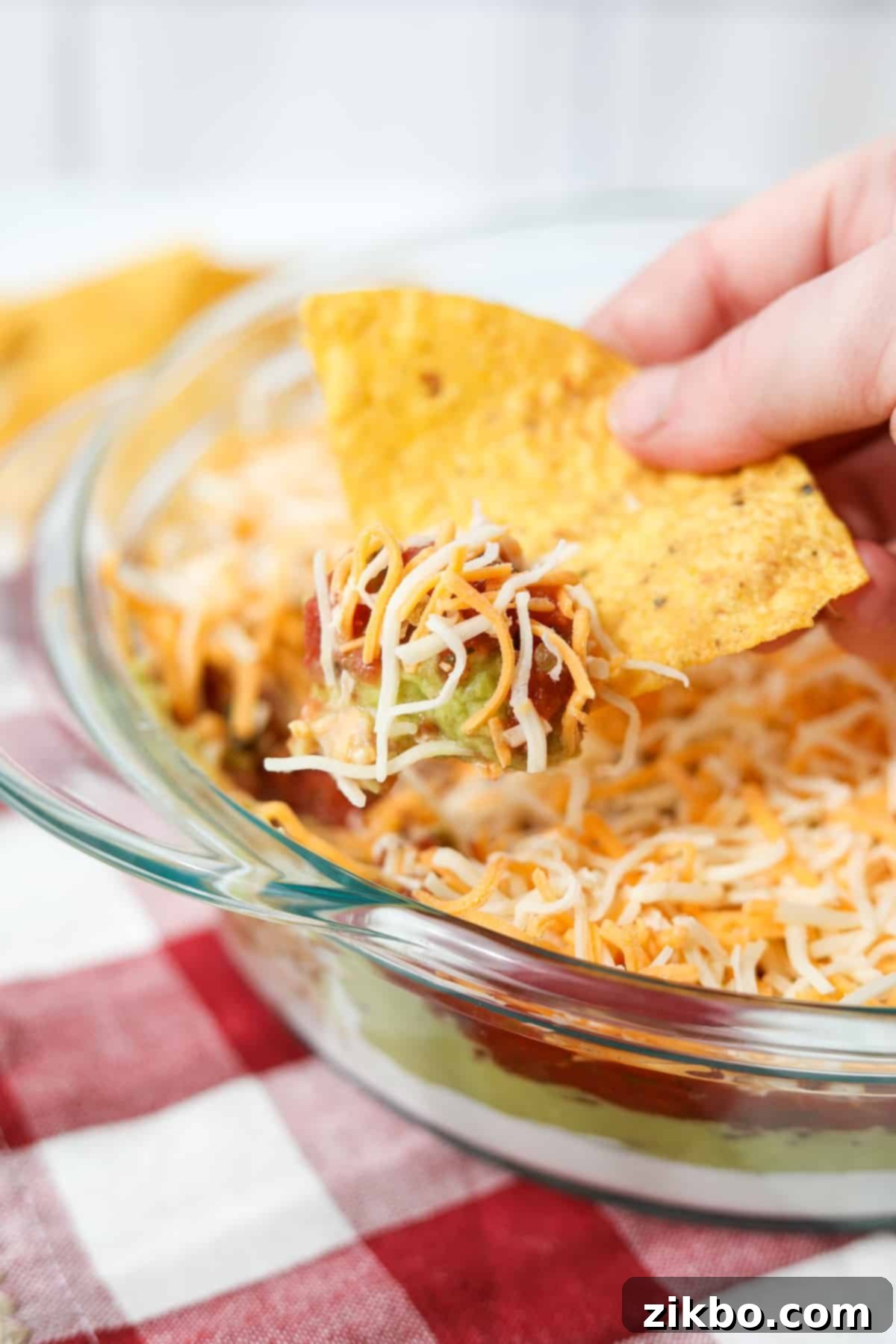 A tortilla chip dipped into a cold layer dip, showing the different layers.