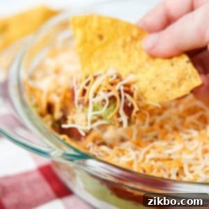 A tortilla chip dunking into a 4 layer dip, highlighting the delicious layers.