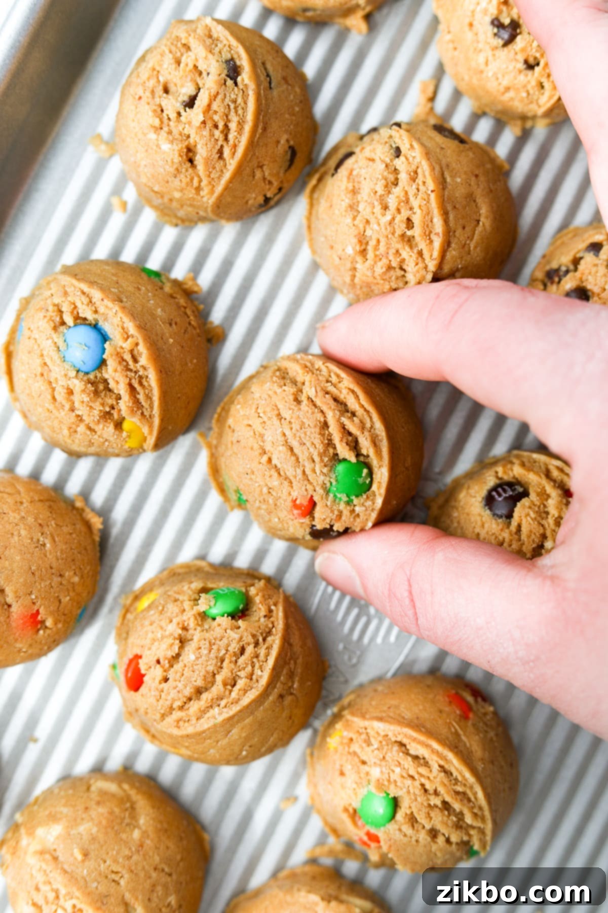 Protein Cookie Dough 12 A hand placing a perfectly formed mound of protein cookie dough onto a baking tray lined with parchment paper.