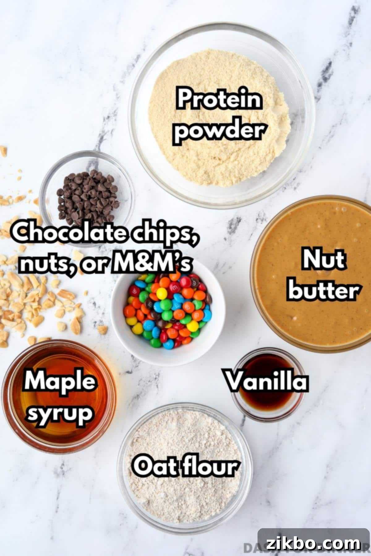 Protein Cookie Dough 3 A selection of ingredients laid out to make protein cookie dough: natural nut butter, vanilla protein powder, maple syrup, oat flour, vanilla extract, and various mix-ins like chocolate chips.