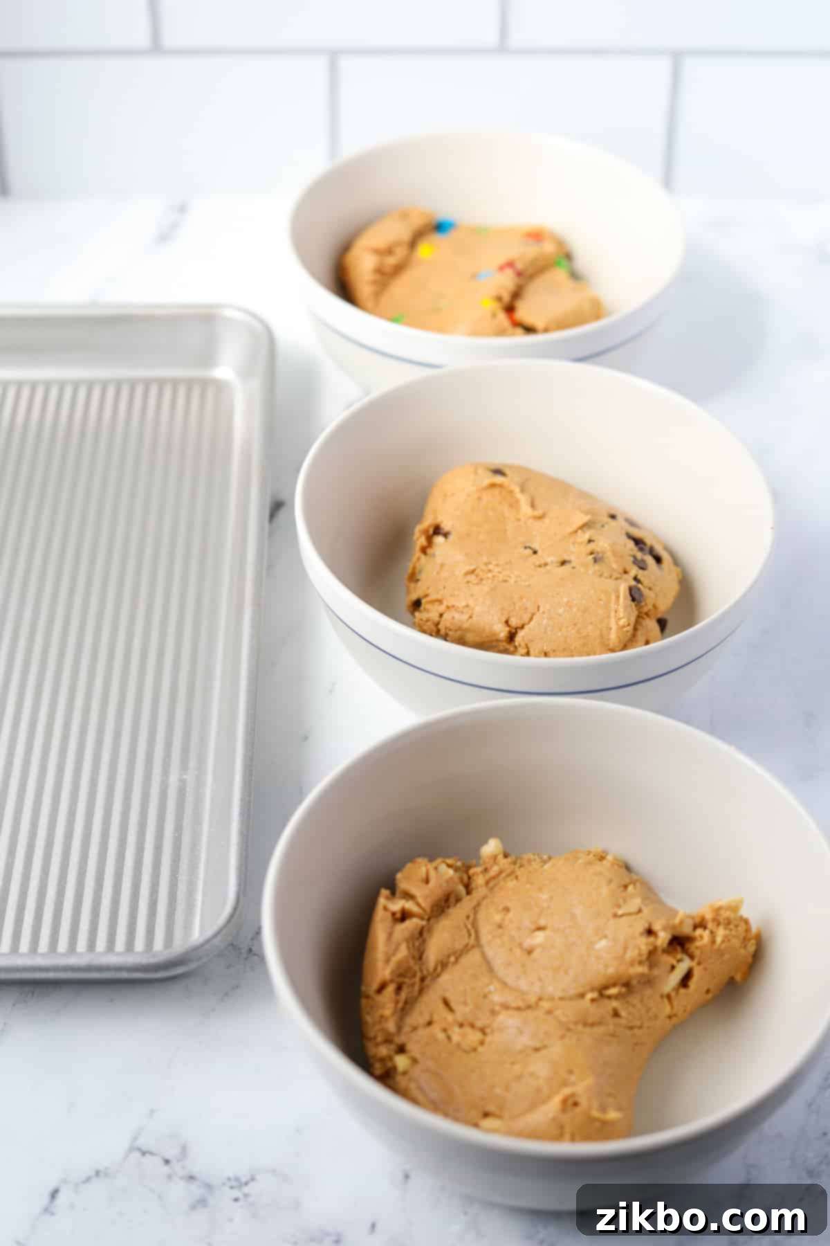 Protein Cookie Dough 7 Three separate bowls of protein cookie dough, each with different mix-ins: chocolate chips, M&M's, and chopped peanuts.