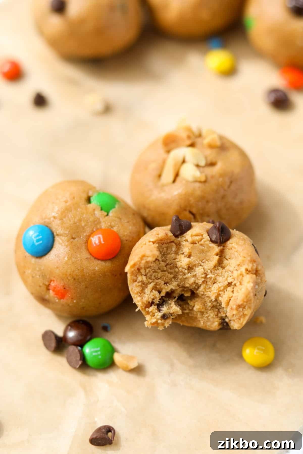 Three cookie dough balls featuring m&m's, chocolate chips, and chopped peanuts.