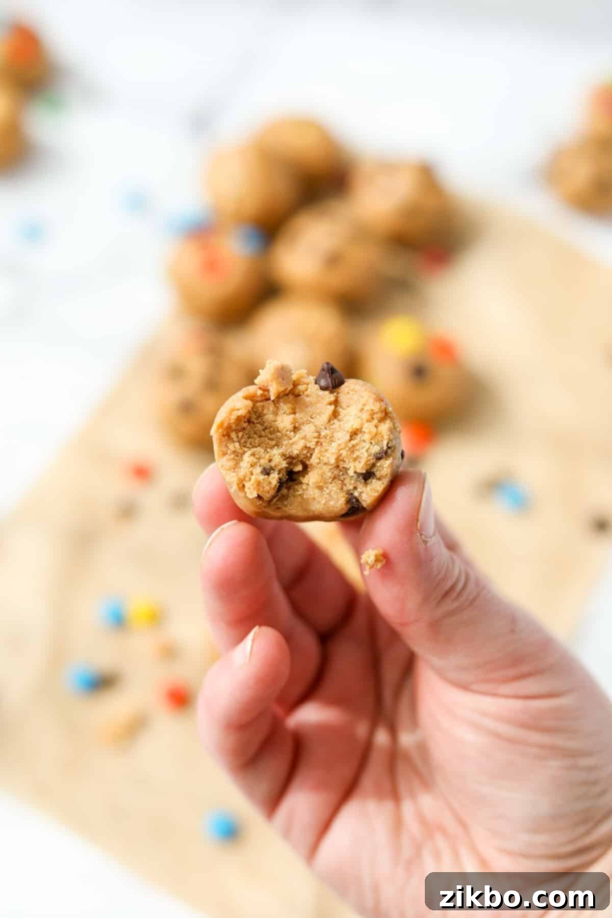 A hand holding up a cookie dough ball with a bite in it.