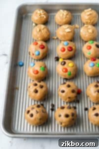 A baking tray with cookie dough balls, featuring chocolate chip, m&m, and chopped peanuts.