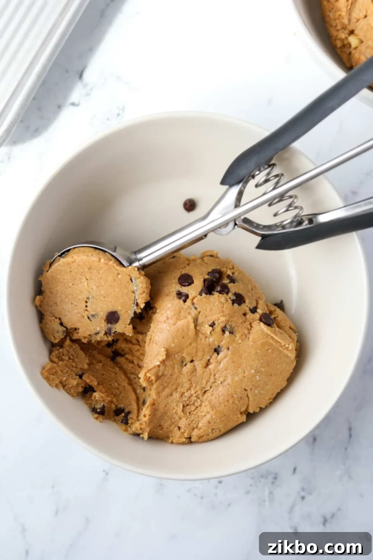 A bowl with protein cookie dough being scooped by a cookie scoop.
