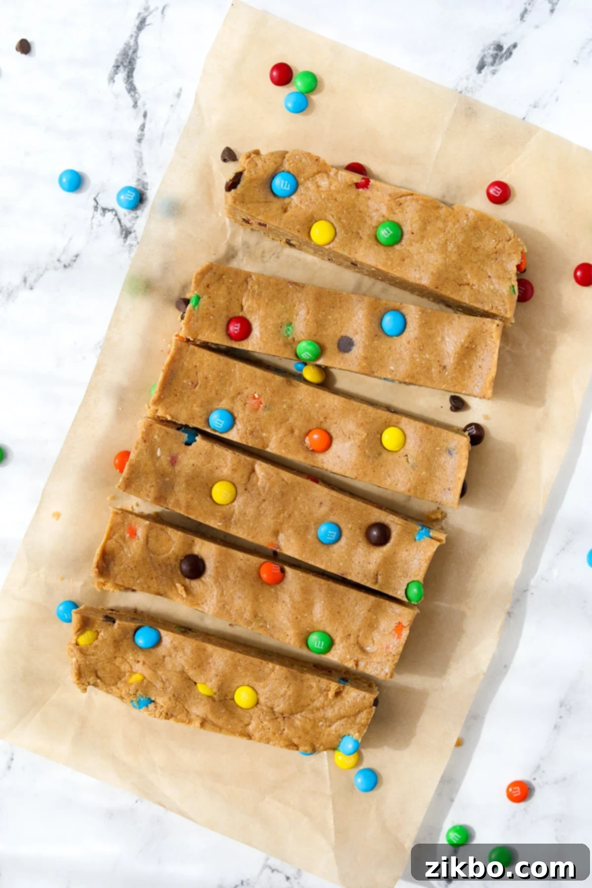 Protein-Packed Monster Cookie Bars 2 6 protein bars on a sheet of unbleached parchment paper, showcasing their colorful M&M and chocolate chip toppings.