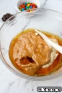 Stirring together a protein cookie dough mixture in a bowl, showing the initial combination of ingredients.