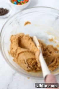 A thick protein cookie dough being mixed thoroughly in a bowl, achieving a smooth and even consistency.
