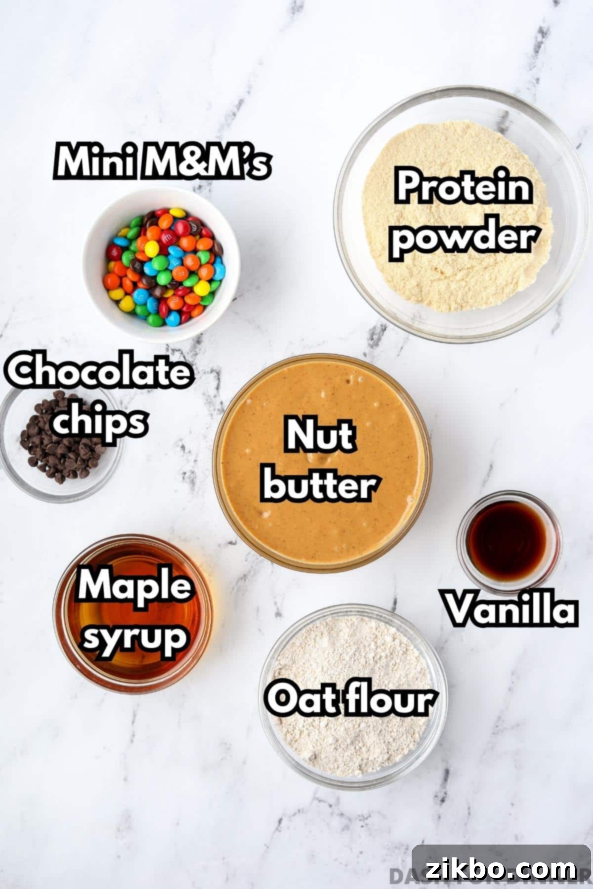 Protein-Packed Monster Cookie Bars 3 An overhead view of different bowls with various ingredients for monster cookie protein bars, including natural peanut butter, vanilla protein powder, mini M&M's, chocolate chips, and maple syrup.