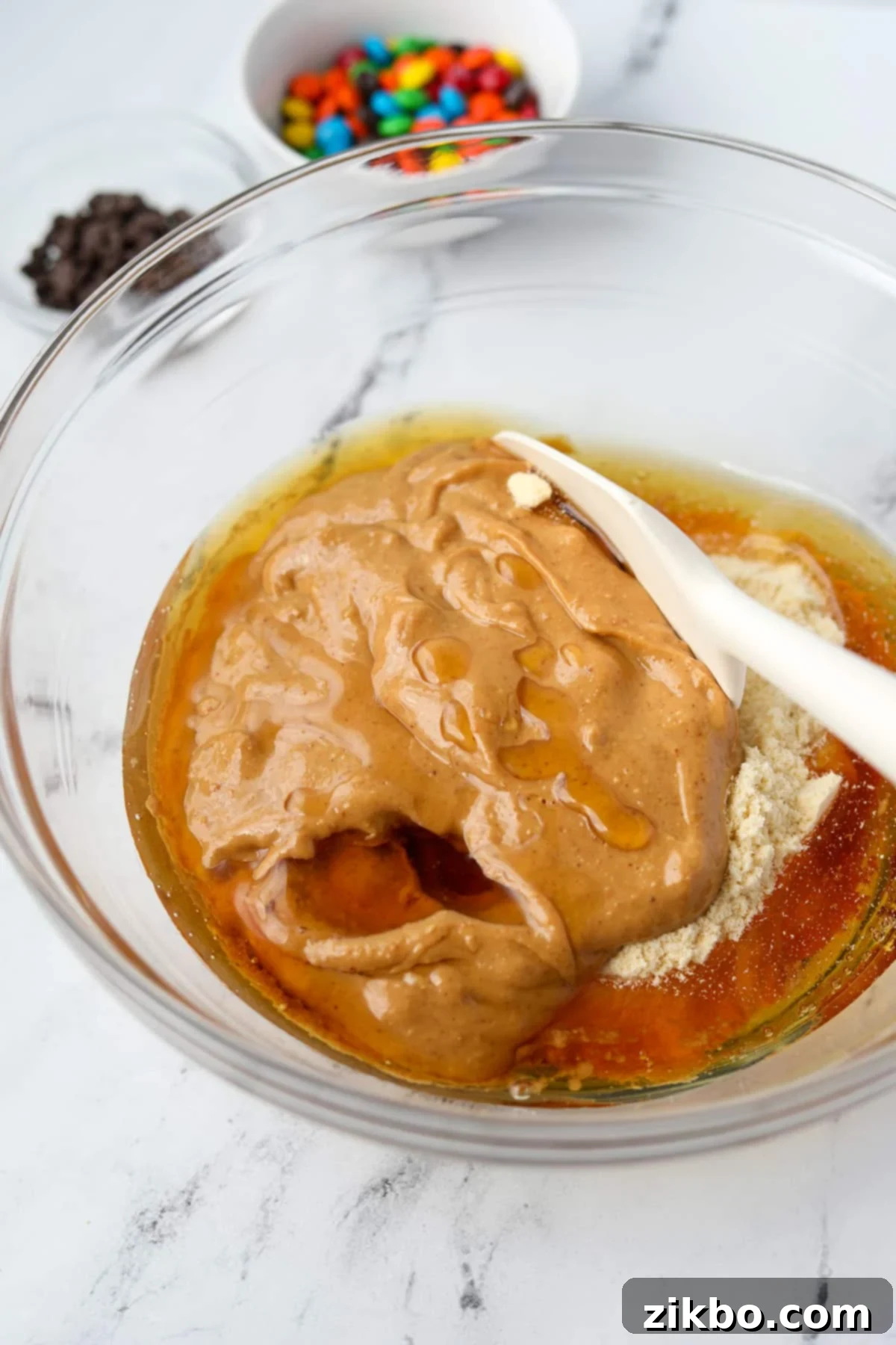 Protein-Packed Monster Cookie Bars 5 A silicone spatula stirring together a thick protein cookie dough mixture in a bowl.