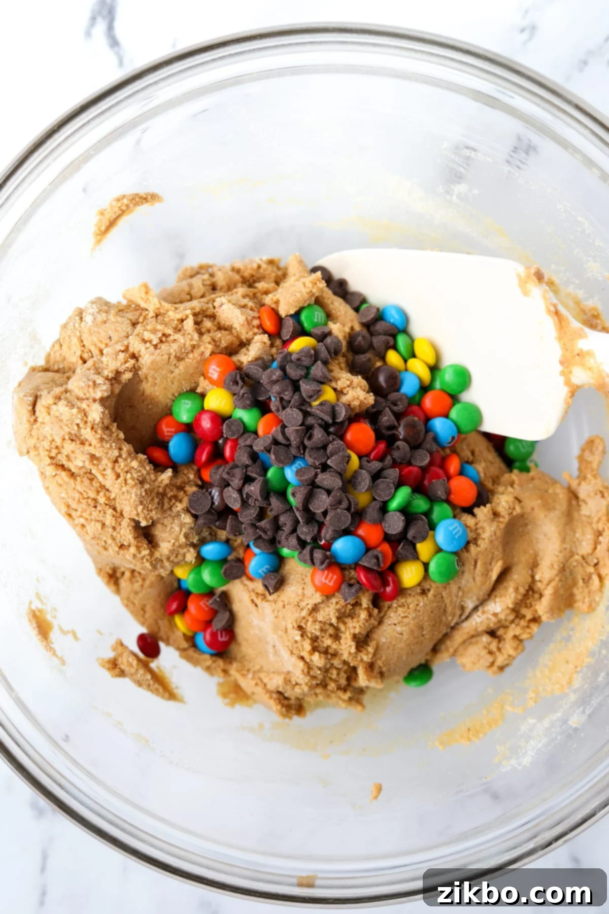 Protein-Packed Monster Cookie Bars 7 Mini M&M's and chocolate chips being folded into a protein cookie dough mixture.
